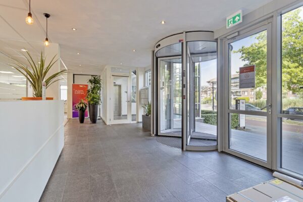 Moderne entreehal van een kantoorpand aan de Fascinatio Boulevard met draaideur, planten en strakke inrichting.